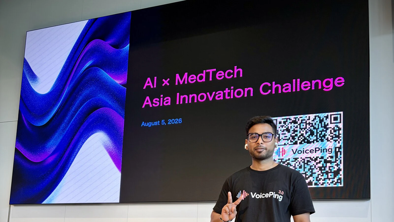 AI×MedTechのイベント表示と来場者向けアクセス用QRコードの前に立つVoicePingのAkash。