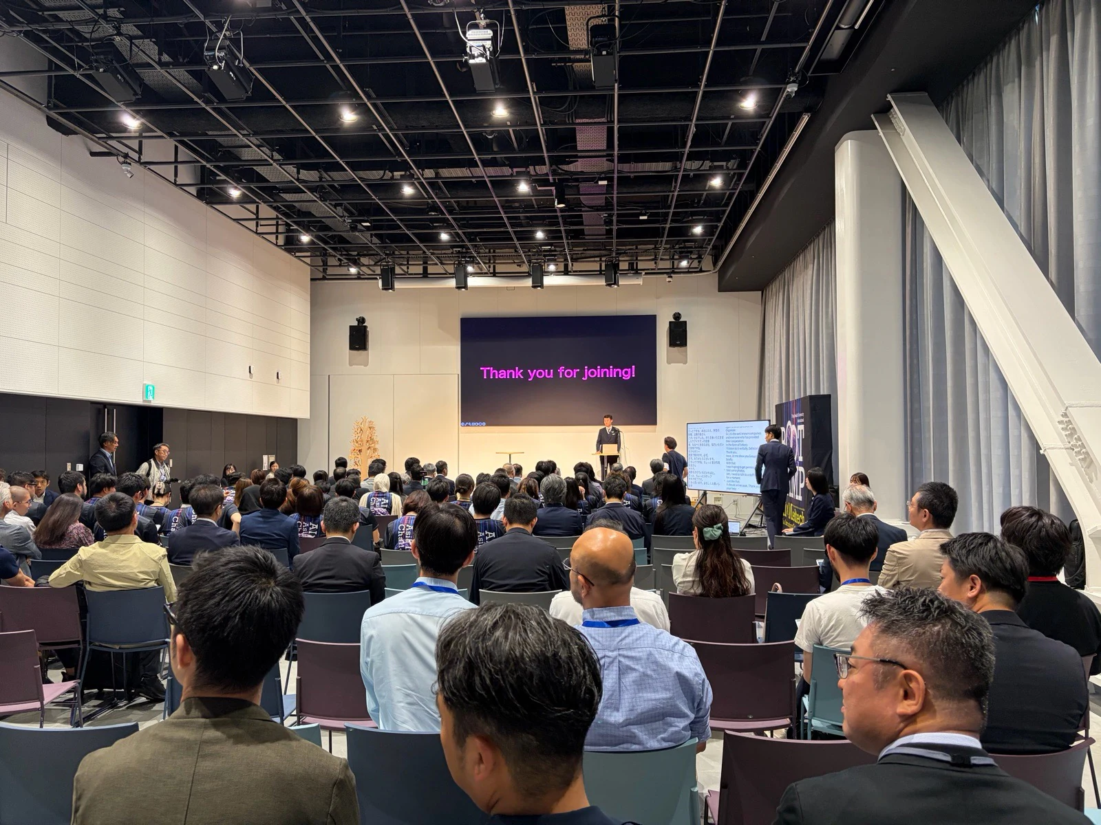 STATION AiでAI×MedTechのメインステージと隣接する二言語字幕画面を見る来場者。
