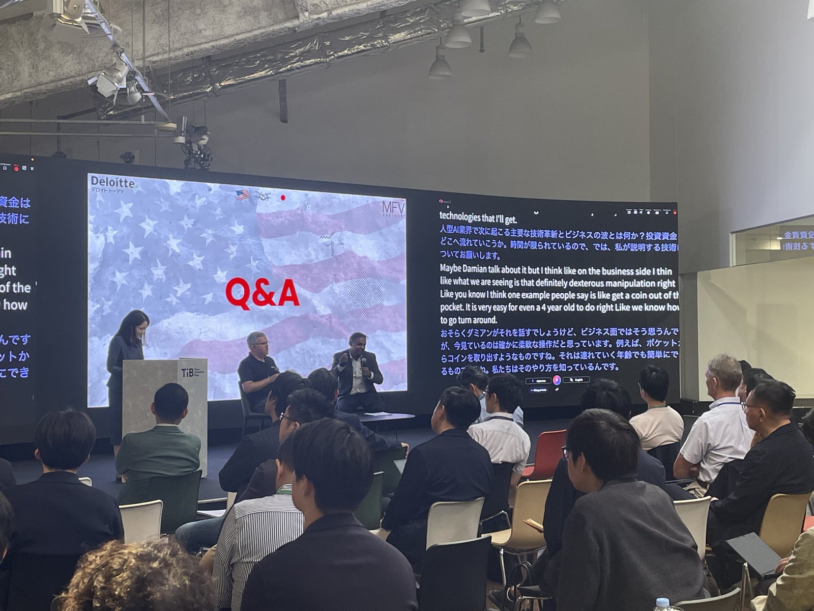 ライブ質疑応答の様子。Q&A のスライドの下で登壇者が着席し、隣のスクリーンに VoicePing のリアルタイム日英翻訳パネルが流れている。