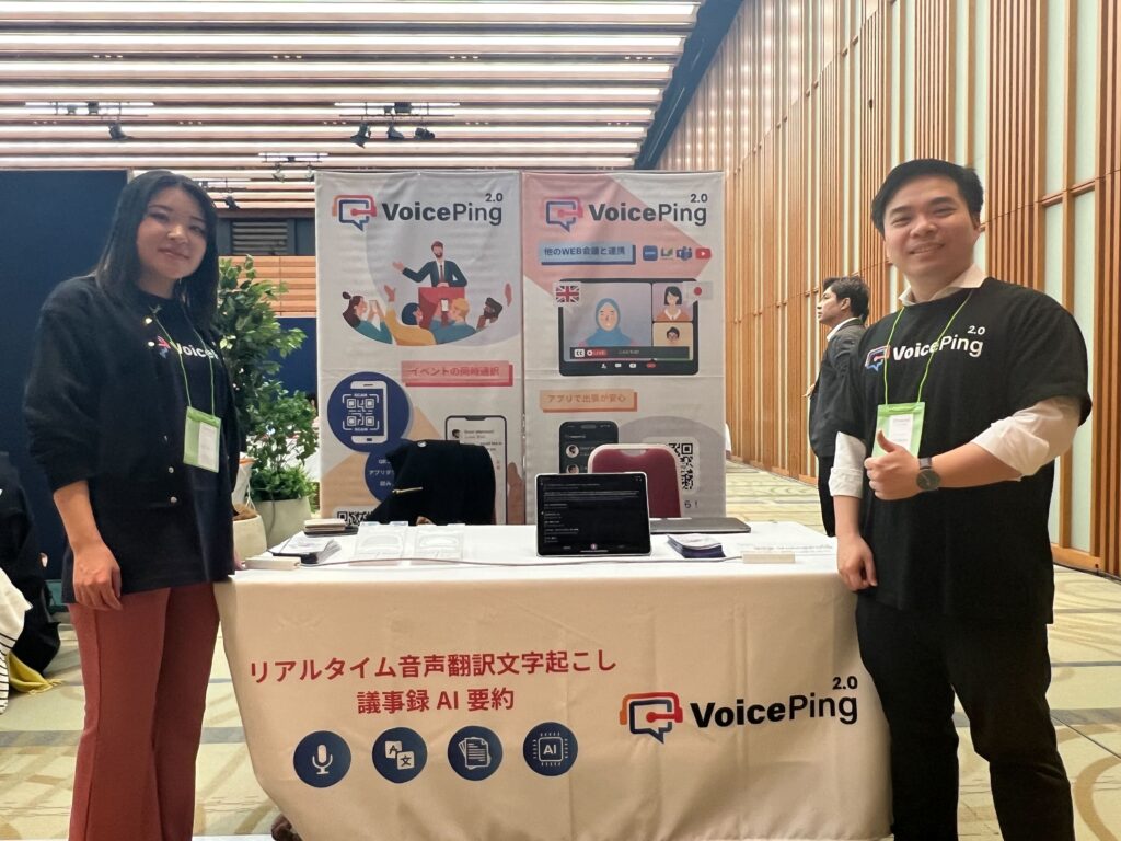 01Booster Conference 2023の展示ブースに立つVoicePingのメンバー2人