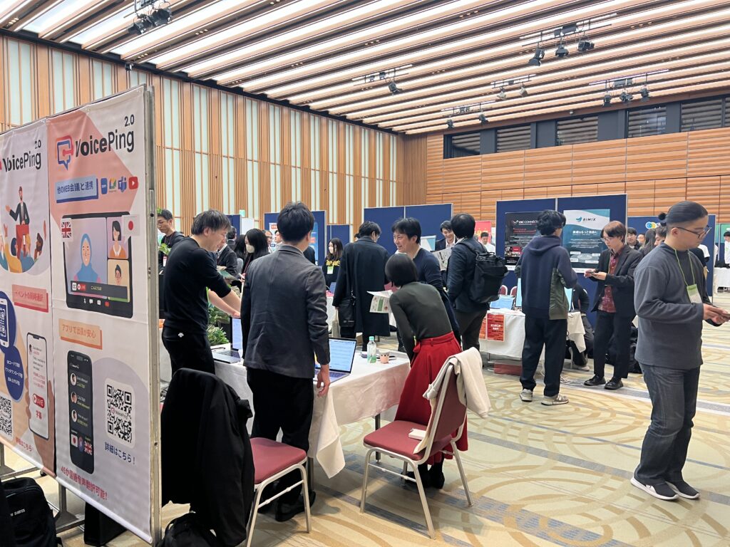 経団連会館の展示スペースで、VoicePingスタッフが来場者に画面を見せながら説明する様子