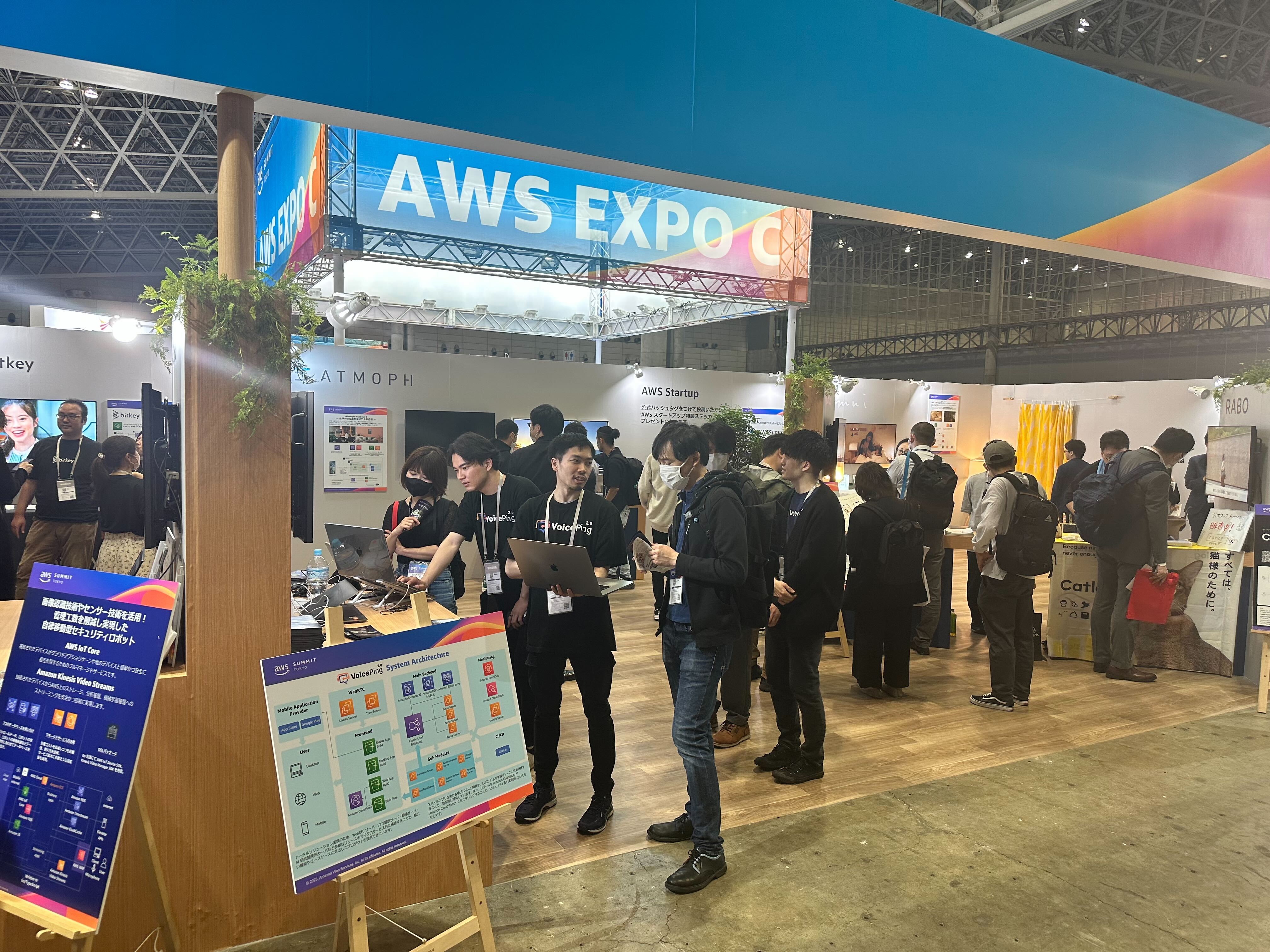 VoicePingスタッフがノートPCを手に来場者へ説明し、手前にシステム構成のパネルが置かれたブース
