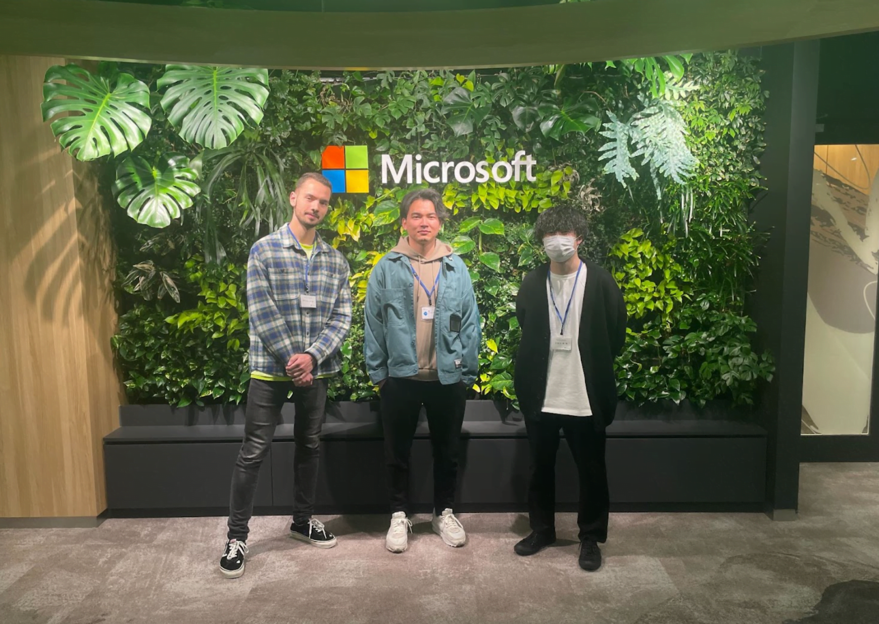 Microsoftのロゴがある壁の前に立つ、OpenHackに参加したVoicePingのメンバー3名