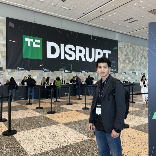 TechCrunch Disruptのロゴがある受付エリアに立つ参加者の山田