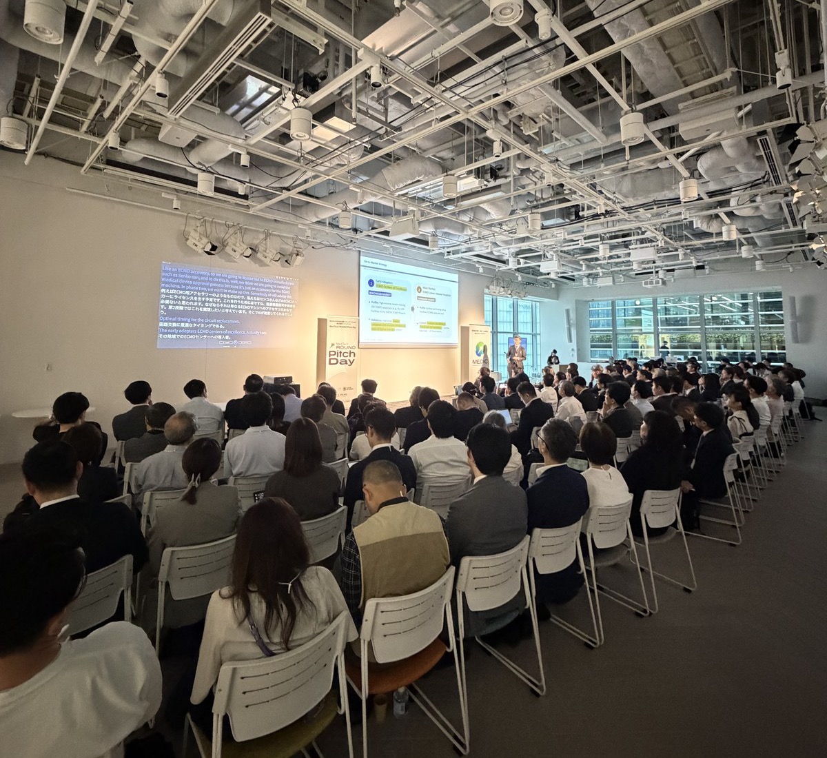MedTech ROUND Pitch Day で、満席の会場がピッチに耳を傾ける様子。前方のスクリーンにはリアルタイム翻訳。