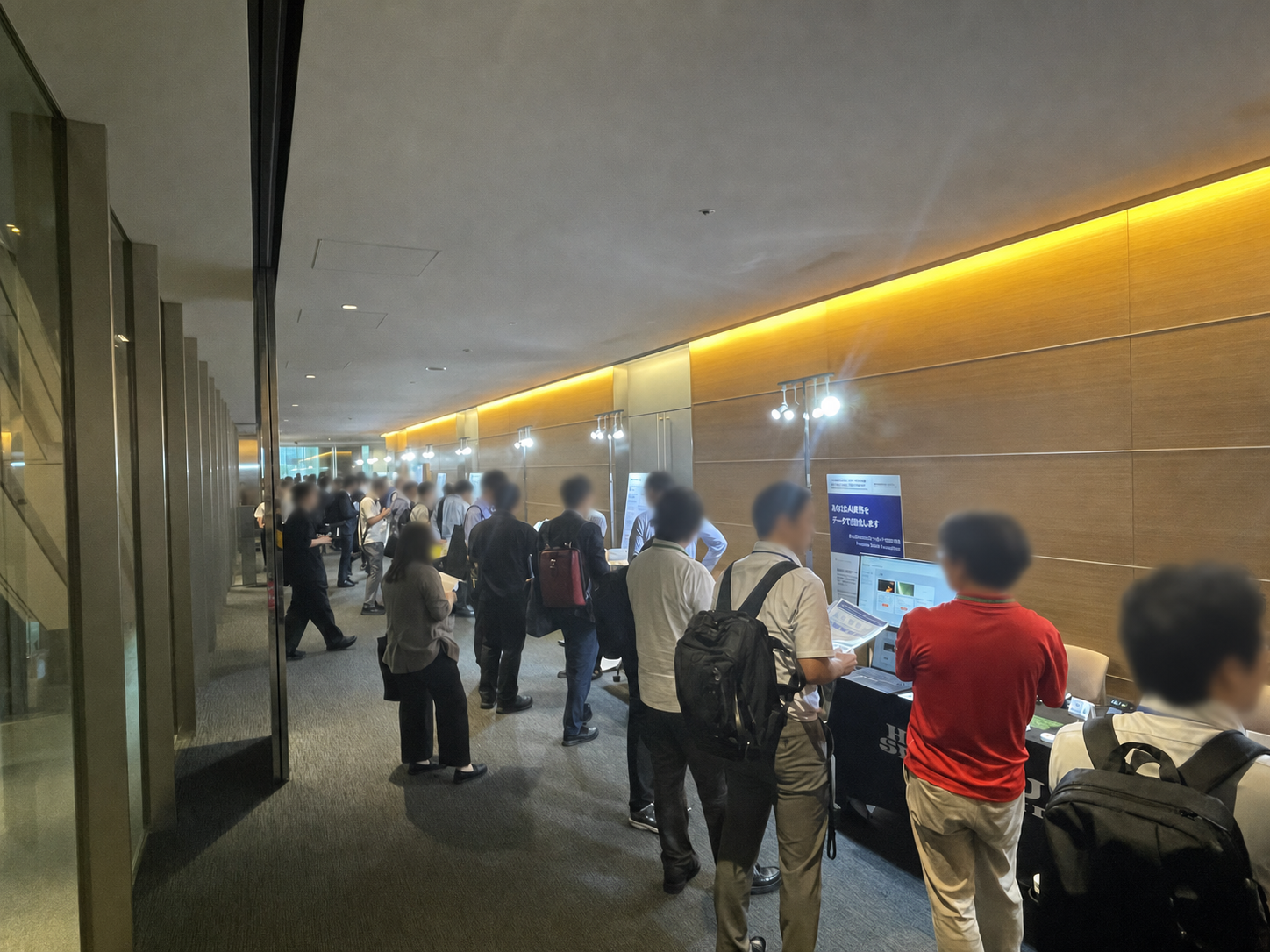 Sony Open Innovation Day 2026の展示通路で出展者と話す参加者。ステージ外で識別可能な顔にはすべてぼかし処理が施されている。