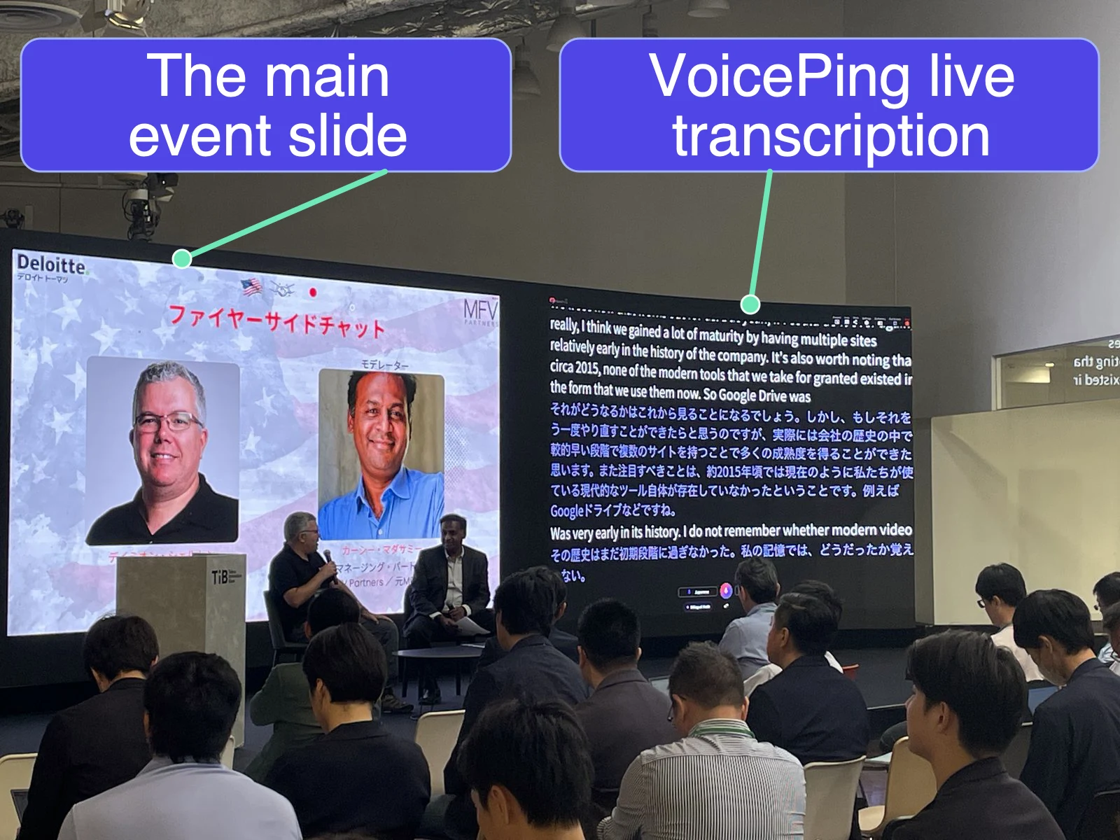 Two speakers hold a fireside chat beside screens showing the event slide, English speech, and live Japanese translation